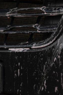 Araba temizleme ayrıntıları, araç yüzeyinin kapatılması, su ve sabun da dahil olmak üzere şehir araba temizliği, sabun köpüklerini ve damlacıkları parlak boyalı araç yüzeyinde gösteren kapalı görüntü