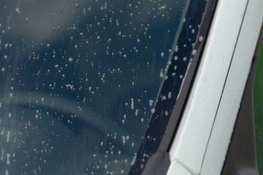 Ön camın köpükle temizlenmesi, sabunlu araba penceresinin detaylı görüntüsü ve yansımaları, temizleme işlemi sırasında köpük ve yansımalarla kaplı araç penceresini gösteren fotoğraf