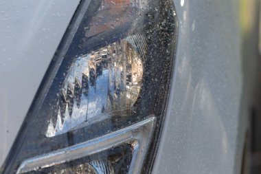 Damlacıklı beyaz araba farları, yumuşak ışık ve yüzey dokusunu yansıtan ıslak mercekler, ince su boncukları ve ince parıltılar, yağmurlu hava ve görüş mesafesi, güvenlik için uygun.