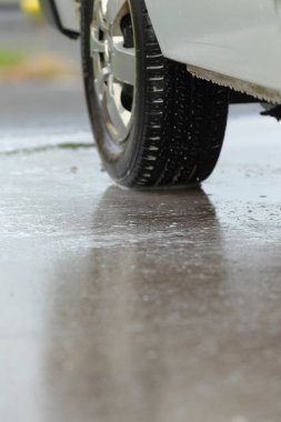 Su dolu tekerlek ve lastik pürüzsüz asfaltta, su yansıması ve sprey efektli lastiğin detaylı görüntüsü, Makro görüntüsü su yansıması ve yol kenarı spreyiyle ıslak lastik izi yakalıyor.