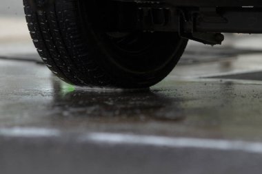 Yansıtıcı ıslak yüzey, parıldayan su birikintisi tekerlek yansımasını gösteriyor, nemli zemin aynaları dönen çarkı açıkça yansıtıyor, parlak ıslak zemin dönen çarkı canlı ve net bir şekilde yansıtıyor.