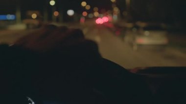 Aydınlatılmış şehir yollarında dikkatle ve dikkatle gezinen dikkatli sürücü, gergin bir odak ile gece saatlerinde ışıltılı kentsel caddelerde gezer.