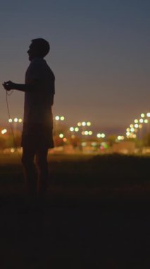 Gün batımı parkı silueti serbest stil ip atlama neşeli ritim, sıcak şehir ışıkları arkasında, anlamlı hareket ve vücut akışı, günlük açık oturum harmanlama dans ve kardiyo