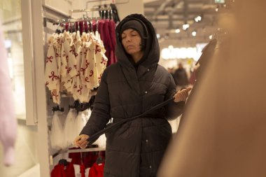 Kış gardırobunu özenle düzenleyen kadın, kişisel stilistlik havası ile alışveriş yapan kadın, raftan ceket ve giysileri koordine ediyor, siluetleri ve dokuları kontrol ediyor, renkleri ve katmanları karıştırıyor,