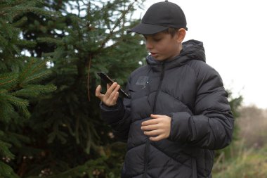 Mobil ekranı yapraklı ortamın yakınındaki konsantrasyonla kontrol eden genç adam, dışarıda doğal güneş ışığıyla rahat bir ortamda akıllı telefon ekranını dikkatle izliyor.