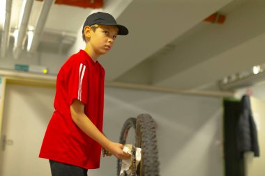 Genç adam patlak lastiği tamir ediyor, kırmızı tişörtlü genç patlak bisiklet tekerleğini tamir ediyor, kırmızı bluzlu genç adam garajda patlak bisiklet lastiğini ustalıkla tamir ediyor.