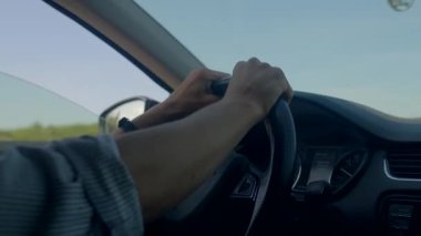 Kafkasyalı kurye yoğun yolda ilerliyor, elleri sıkıca kavrıyor, geçen kamyon ve evler görünür durumda, uyanık duruş, banliyö trafiği, savunmacı sürüş havası ve gösterge paneli manzarası.