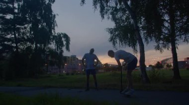 Günbatımında egzersiz yapan arkadaşlar, akşam parkında aktif arkadaşlar, doğada birlikte çalışan insanlar, gün batımında yeşil ortamda fiziksel aktivite yapan iki kişi.