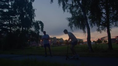 Erkek koç, şehir parkında gün batımına yardımcı oluyor, yol gösterici, nazik rehberlik, alacakaranlık silueti, ağaçların çerçevelenme sahnesi, akşam antrenmanı sırasında esneklik ve uygun forma odaklan.