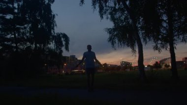 Günbatımında şehir parkında koşan siluetli erkek, yalnız erkek sporcu şehir parkı ortamında akşam koşusunun keyfini çıkarıyor, yalnız erkek gün batımında şehir parkı yolunda koşuyor ve koşusuna odaklanıyor.