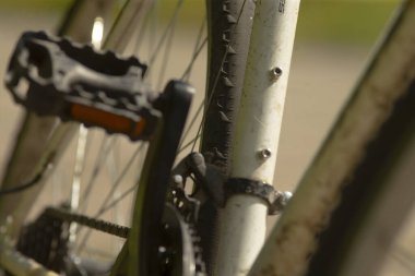 Kapalı bisiklet kolu ve zinciri yağ ve aşınmayı gösteriyor, metal dişler ve çıkıntı ayrıntıları, güneş ışığı çizikleri ve deseni olan şehir içi banliyö havası..