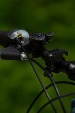 Çan ve kabloyla yakın bisiklet gidonu, yumuşak yeşil arka planda siyah gidon ve gümüş zil, fren kolu ve metal dokular vurgulandı, sığ derinlik ve bokeh oluşturuldu