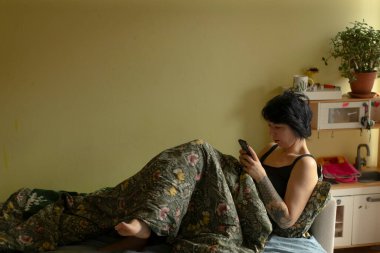 Kadının dijital içerikle etkileşimi, bitki ve balkonla rahat bir akşam sahnesi, bitki ve balkon dekoru arasında mesajlaşan bir kadının yer aldığı sakin bir akşam ortamı