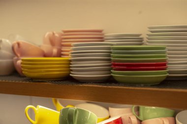 Pastel fincanlar ve tabaklar mutfak rafında, restoran içi depolama kabı katmanlı sarı, pembe ve yeşil çanak çömlek, günlük cazibeyle, sahne öğle vakti stoklama ve düzenli önerir