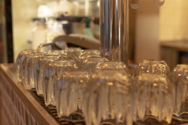 Tezgahta yansıtıcı cam sıra, restoranın içi cilalı yüzeyler ve yumuşak röfleler, ışığı yakalayan düzgün ters çevrilmiş taklacılar, ince bir arkaplan ile hizmetten önce sakin bir sahne