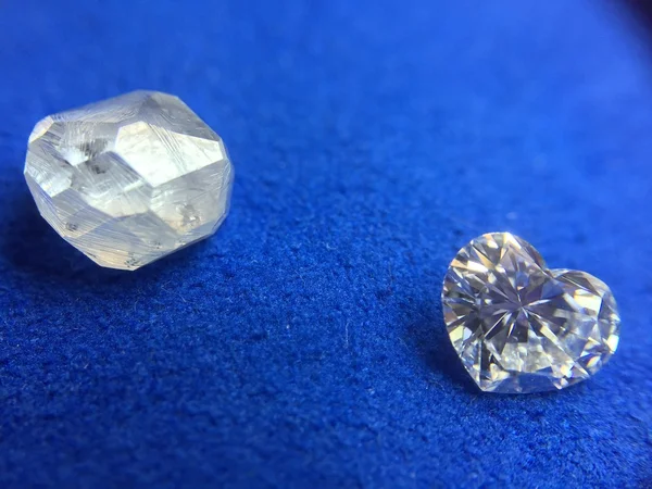 Rohdiamant und Diamant in Herzform auf blauem Tuch Stockbild