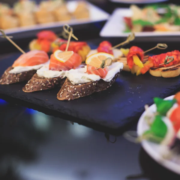 Mesa de banquete de catering lindamente decorada com diferentes lanches e aperitivos de alimentos com sanduíche, caviar, frutas frescas na festa de aniversário de Natal corporativa — Fotografia de Stock