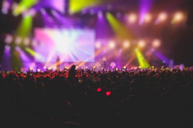 Sahne ışıklarıyla kalabalık bir konser salonu, rock gösterisi performansı, insanların silueti, bir konser festivali sırasında dans pistinde renkli konfeti patlaması.