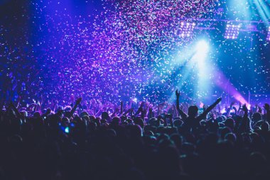 Sahne ışıklarıyla kalabalık bir konser salonu, rock gösterisi performansı, insanların silueti, bir konser festivali sırasında dans pistinde renkli konfeti patlaması.