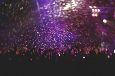 Sahne ışıklarıyla kalabalık bir konser salonu, rock gösterisi performansı, insanların silueti, bir konser festivali sırasında dans pistinde renkli konfeti patlaması.