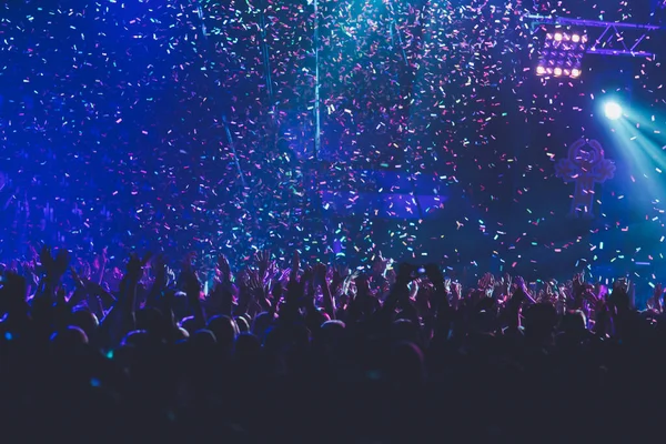 A crowded concert hall with scene stage lights, rock show performance, with people silhouette, colourful confetti explosion fired on dance floor during a concert festival