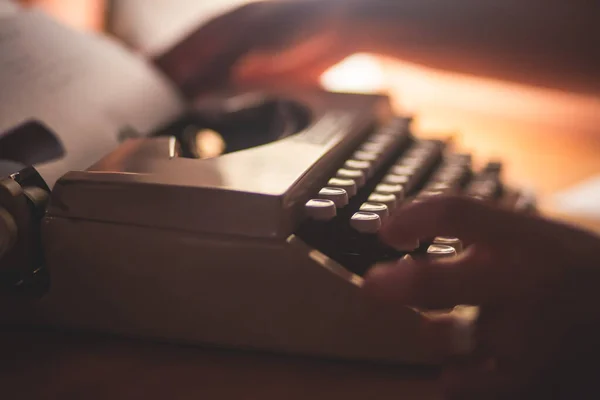 Process of writing a text letter on a white sheet of paper with old-fashioned typewriter, modern writer machine in warm room candle light, close up view of hands writing and printing