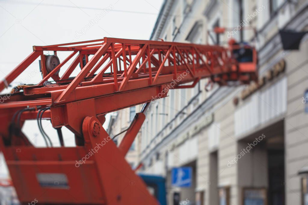 Aerial work platform vehicle during facade decoration, orange telescopic elevator on construction site, rental AWP working in the city streets, engineer working on height