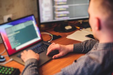 IT geliştirici programcısı evinde, bilgisayarında ve masaüstü monitöründe kodlama programı uygulaması ile çalışıyor ve kodluyor, uzaktan kumanda evden çalışıyor, sıcak akşam resmi