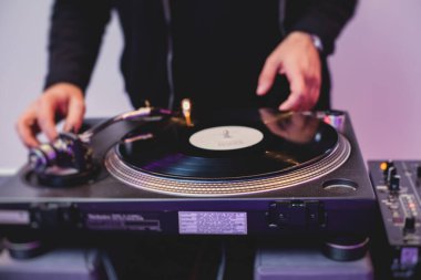DJ 'in çaldığı bir masada DJ' in kulaklığıyla DJ mikseri ve plaka görüntüsü gece kulübündeki tekno partisinde arka planda müziği karıştırıyor.