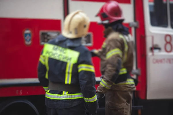 Group of fire men in uniform during fire fighting operation in the city streets, firefighters with the fire engine truck fighting vehicle in the background, emergency