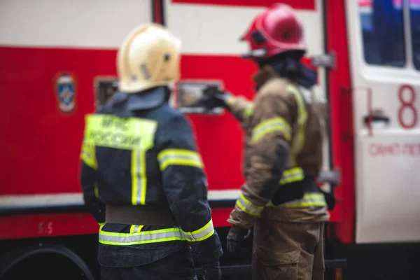 Group of fire men in uniform during fire fighting operation in the city streets, firefighters with the fire engine truck fighting vehicle in the background, emergency