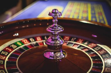 Çok renkli kumarhane masasının canlı bir görüntüsü. Rulet oynanıyor, kumarhane fişleri takılıyor. Krupiye, para ve arka planda oynayan bir grup zengin kumarbazın eli. 