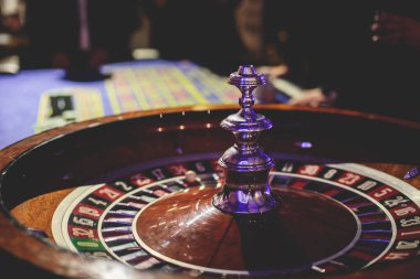 Çok renkli kumarhane masasının canlı bir görüntüsü. Rulet oynanıyor, kumarhane fişleri takılıyor. Krupiye, para ve arka planda oynayan bir grup zengin kumarbazın eli. 