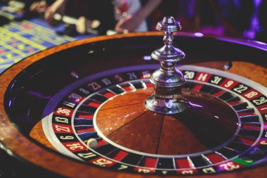 Çok renkli kumarhane masasının canlı bir görüntüsü. Rulet oynanıyor, kumarhane fişleri takılıyor. Krupiye, para ve arka planda oynayan bir grup zengin kumarbazın eli. 