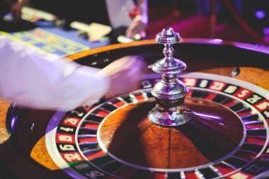 Çok renkli kumarhane masasının canlı bir görüntüsü. Rulet oynanıyor, kumarhane fişleri takılıyor. Krupiye, para ve arka planda oynayan bir grup zengin kumarbazın eli. 