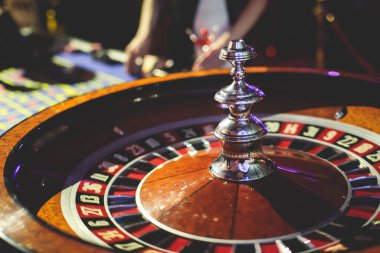 Çok renkli kumarhane masasının canlı bir görüntüsü. Rulet oynanıyor, kumarhane fişleri takılıyor. Krupiye, para ve arka planda oynayan bir grup zengin kumarbazın eli. 