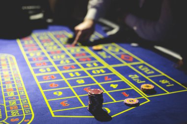 Çok renkli kumarhane masasının canlı bir görüntüsü. Rulet oynanıyor, kumarhane fişleri takılıyor. Krupiye, para ve arka planda oynayan bir grup zengin kumarbazın eli. 