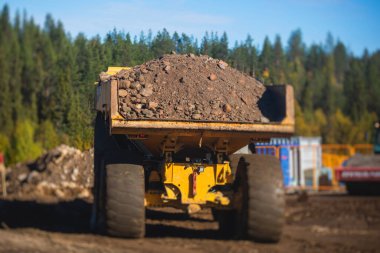 Sarı ağır kazıcı ve çöp kamyonu bahşişçisi kum kazıyor ve yol çalışmaları sırasında çalışıyor, etrafta işçilerin olduğu yeni bir yolun inşaatı sırasında kum boşaltıyor