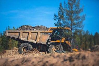 Sarı ağır kazıcı ve çöp kamyonu bahşişçisi kum kazıyor ve yol çalışmaları sırasında çalışıyor, etrafta işçilerin olduğu yeni bir yolun inşaatı sırasında kum boşaltıyor