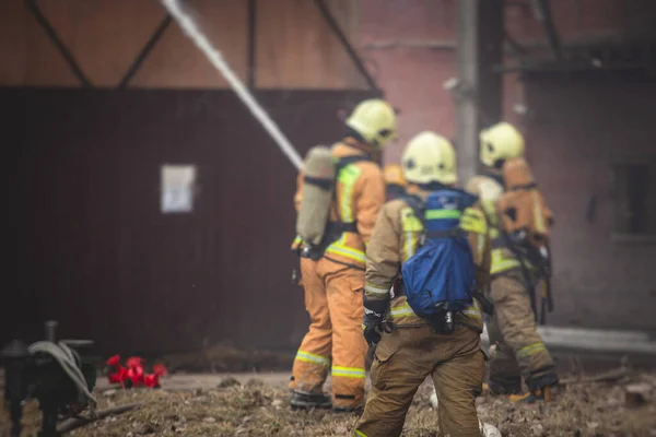 Firefighters put out large massive fire blaze, group of fire men in uniform during fire fighting operation in the city streets, firefighters with fire engine truck fighting vehicle