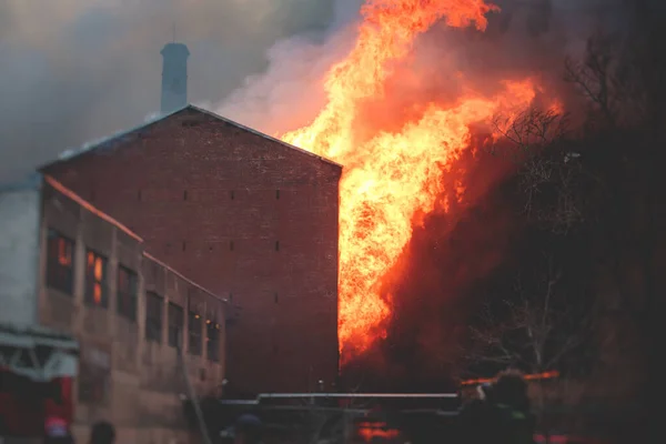 Massive large blaze fire in the city, brick factory building on fire, hell major fire explosion flame blast,  with firefighters team firemen on duty, arson, burning house destruction