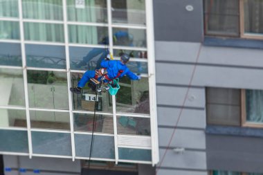 Yüksek binaların camlarını temizleyen profesyonel tırmanma halatı işçisi, endüstriyel dağcılar modern bir binanın cam cephesini yıkıyorlar, yüksek yerlerde çalışmak riskli. 