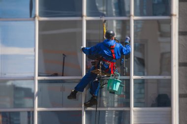 Yüksek binaların camlarını temizleyen profesyonel tırmanma halatı işçisi, endüstriyel dağcılar modern bir binanın cam cephesini yıkıyorlar, yüksek yerlerde çalışmak riskli. 