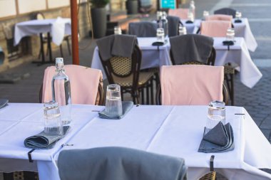 Avrupai yaya caddesinde boş bir sokak kafe restoranı manzarası, sandalyeler, masalar beyaz masa örtüsü, pembe ve gri battaniye, şişeler 