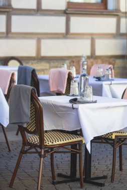 Avrupai yaya caddesinde boş bir sokak kafe restoranı manzarası, sandalyeler, masalar beyaz masa örtüsü, pembe ve gri battaniye, şişeler 