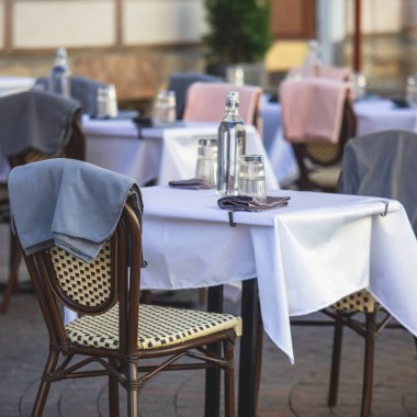 Avrupai yaya caddesinde boş bir sokak kafe restoranı manzarası, sandalyeler, masalar beyaz masa örtüsü, pembe ve gri battaniye, şişeler 