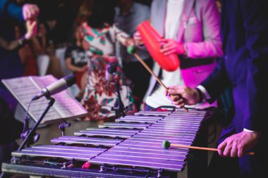 Ksilofon konser görüntüsü vibratör marimba çalar, tokmaklar davul sopaları, arka planda Latin orkestra müzik grubu sahne alacak.