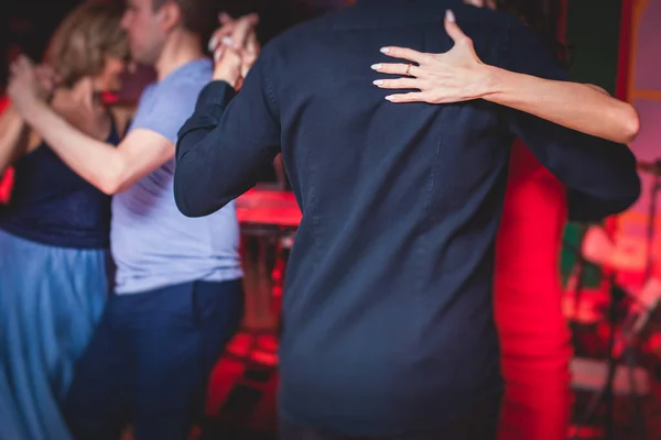 Couples dancing traditional latin argentinian dance milonga in the ballroom, tango salsa bachata kizomba lesson in the red, purple lights, dance festival