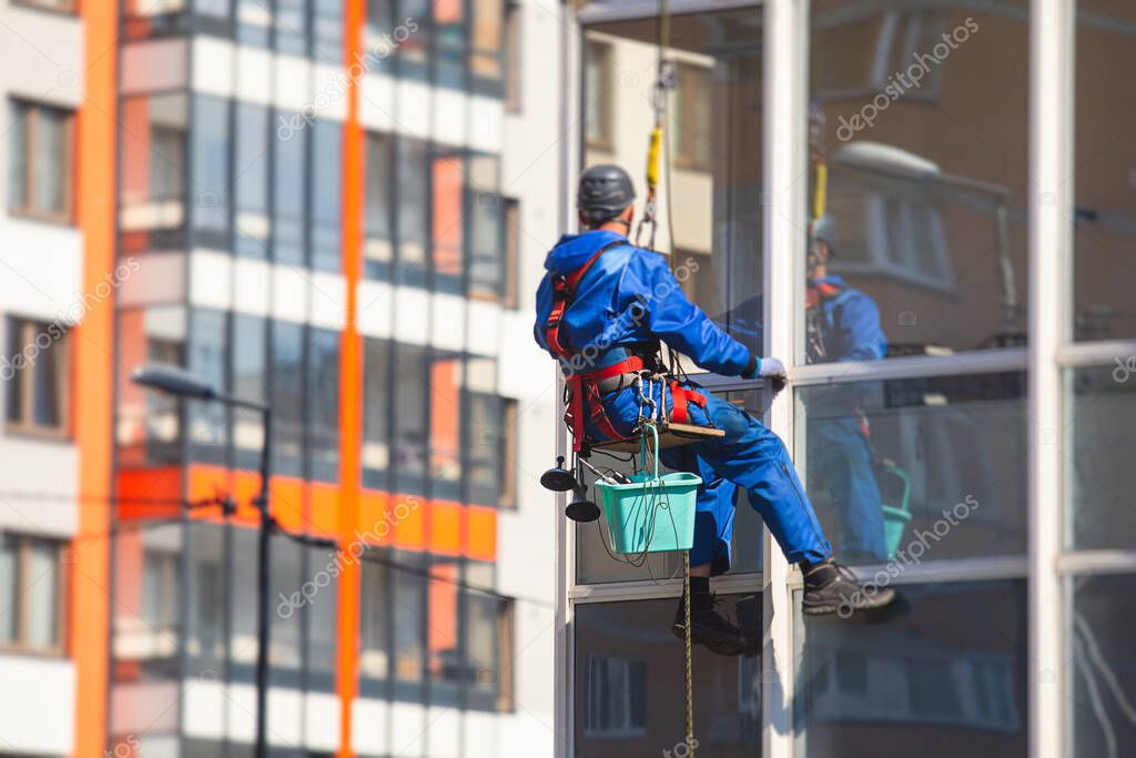 Professional climber rope access worker cleaning the windows on the high rise building, industrial mountaineers washing the glass facade of a modern building, risky working at heights 