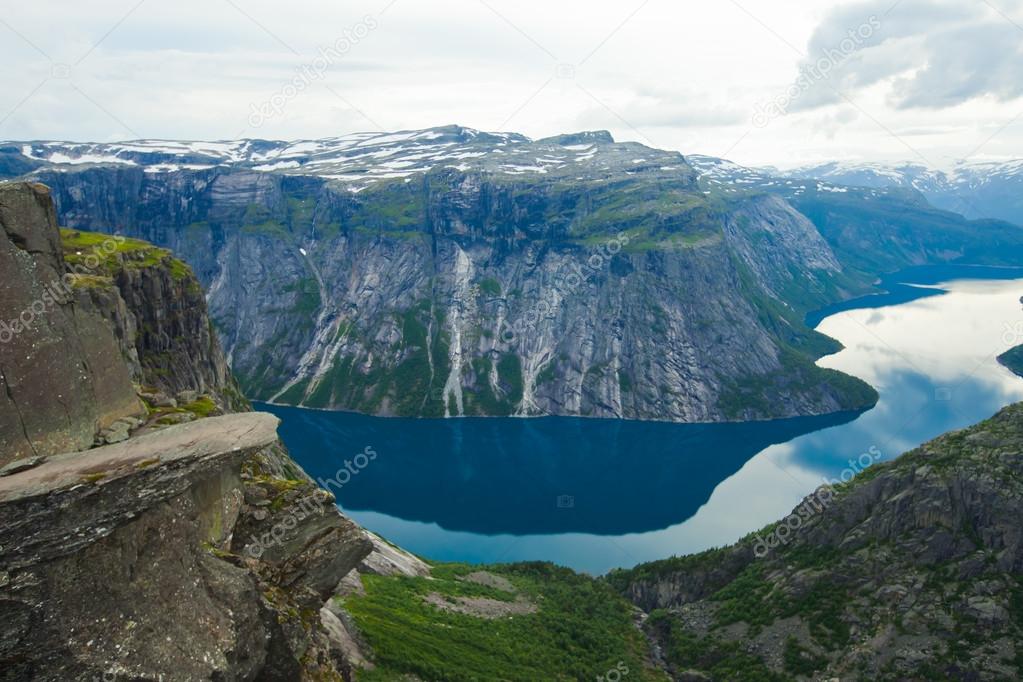 A vibrant picture of famous norwegian hiking place - trolltunga, the trolls tongue, rock skjegedall, with a tourist, and lake ringedalsvatnet and mountain panoramic scenery epic view, Norway